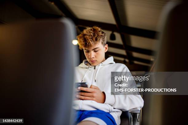 teenager boy is using smartphone at airport waiting zone - concentration curl stock pictures, royalty-free photos & images