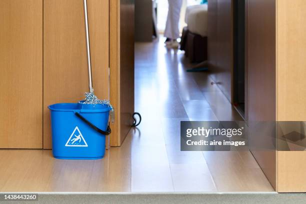 a blue bucket with a mop leaning against a wooden wall next to the door overlooking a hallway. - aljofifa fotografías e imágenes de stock