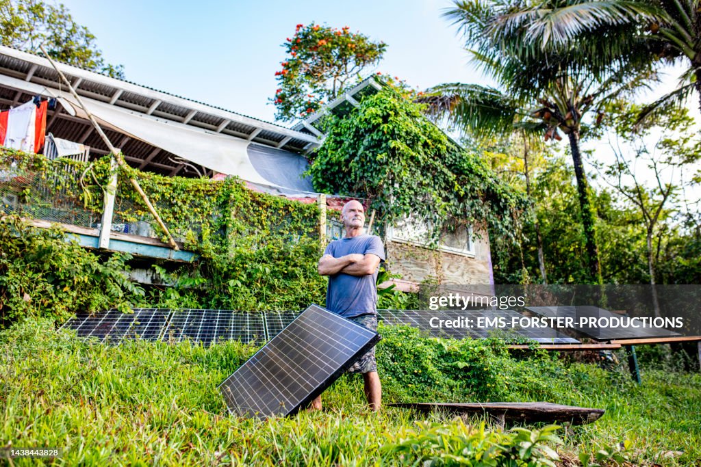 Active, male senior is standing beside his solar panels in his jungle garden