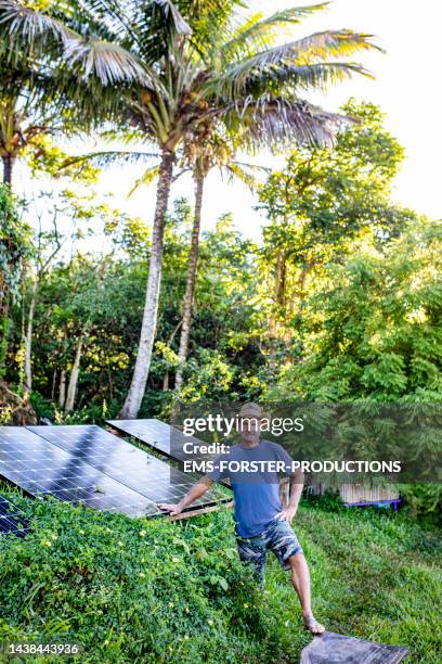 active, male senior is standing beside his solar panels in his jungle garden - autarkie stockfoto's en -beelden