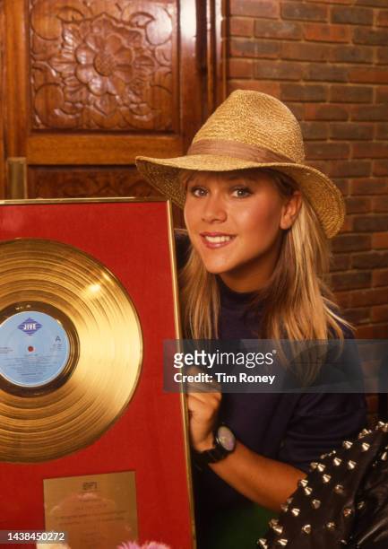 Portrait of British Pop musician Samantha Fox as she poses with a framed gold record commemorating her 'Touch Me' album, circa 1987.