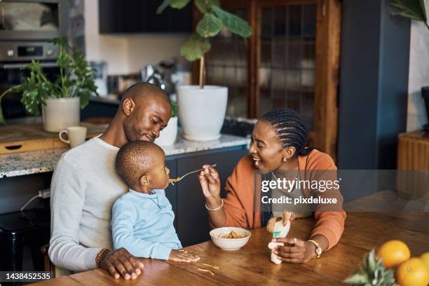 eating, baby and parents with food in the kitchen of their house for breakfast, lunch or dinner. young, happy and mother with smile while feeding a child at a table with love from dad in the morning - baby eating toy stock pictures, royalty-free photos & images