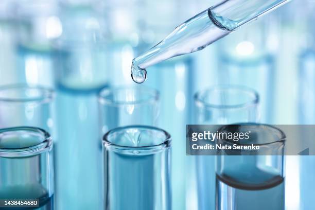 laboratory glassware with dropper dripping liquid into test tube with light blue liquid close up macro photography. - laboratório imagens e fotografias de stock