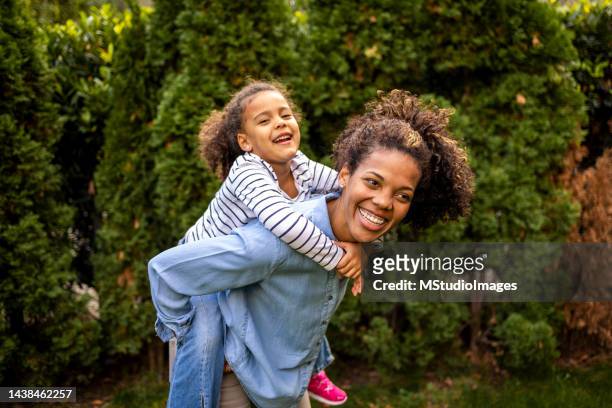 african american mother and daughter playing piggyback outdoors - cuban ethnicity stock pictures, royalty-free photos & images