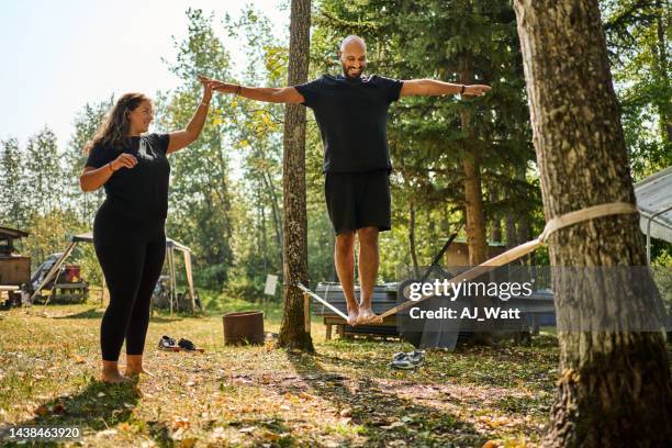 lächelnder junger mann beim slacklinen draußen mit seiner freundin - slacklining stock-fotos und bilder