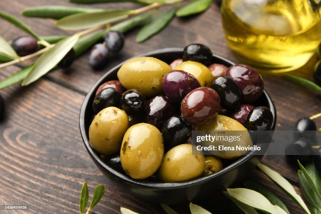 Different kinds of olives in olive oil with herbs on a wooden background with olive tree branches