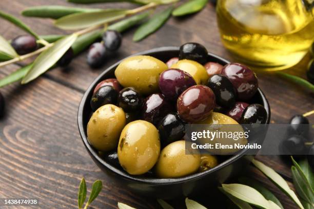 different kinds of olives in olive oil with herbs on a wooden background with olive tree branches - olive stock pictures, royalty-free photos & images