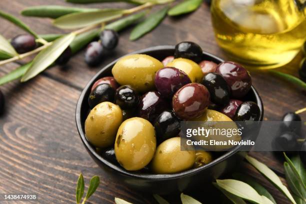 different kinds of olives in olive oil with herbs on a wooden background with olive tree branches - olive 個照片及圖片檔
