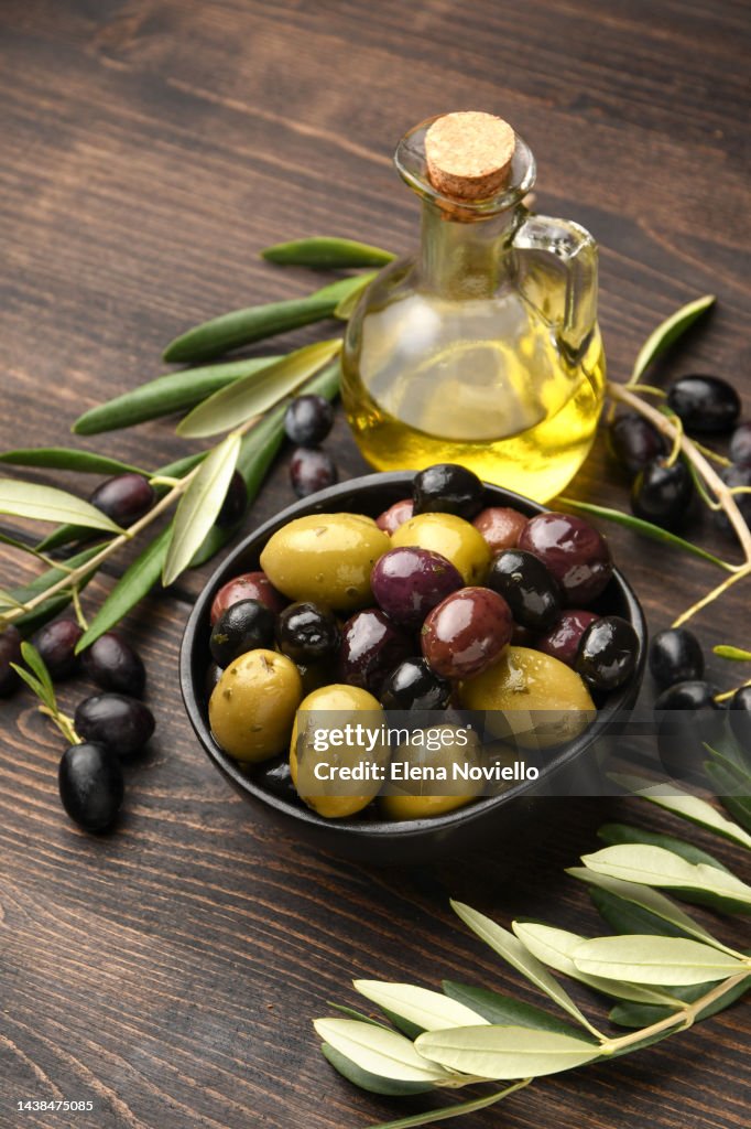 Different kinds of olives in olive oil with herbs on a wooden background with olive tree branches