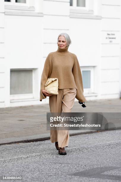 Best ager model Petra van Bremen wearing a beige knitted cashmere turtleneck pullover by Khaite, beige wide leg pants by Seductive, brown leopard...