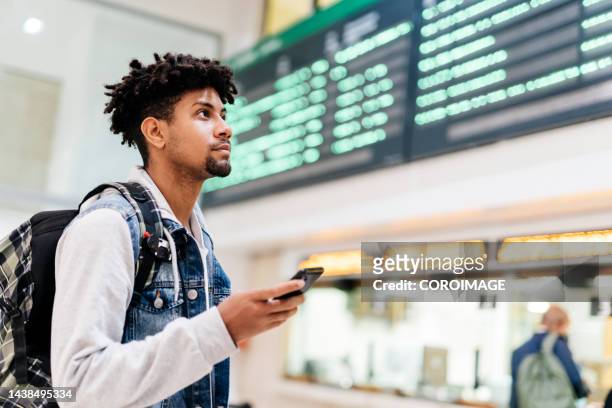 young man at the airport looking at the list of destinations holding a cell phone. - travel fotografías e imágenes de stock