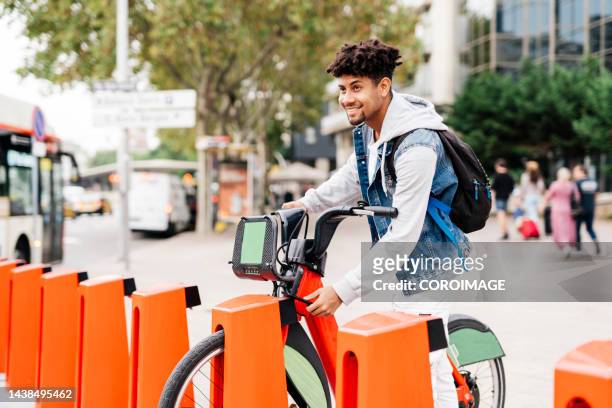 young man using smart phone to pick up a bike on the street. - sustainable transportation stock pictures, royalty-free photos & images