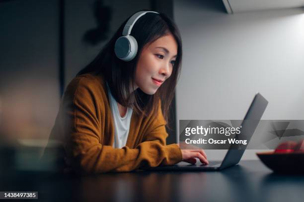 young asian woman with headphone, studying online with laptop at home during the night - asian watching movie stock-fotos und bilder