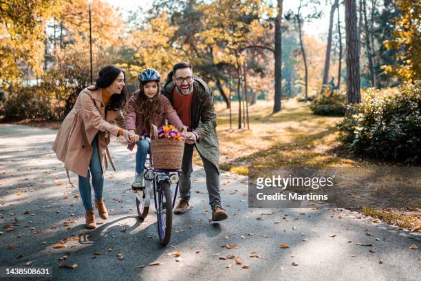 parents teaching daughter how to ride bicycle - child and parent and bike stock pictures, royalty-free photos & images