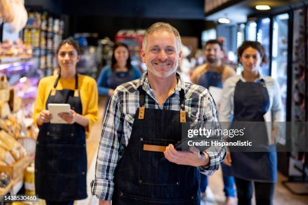 happy business owner with a group of workers at his food shop - convenience store stock pictures, royalty-free photos & images