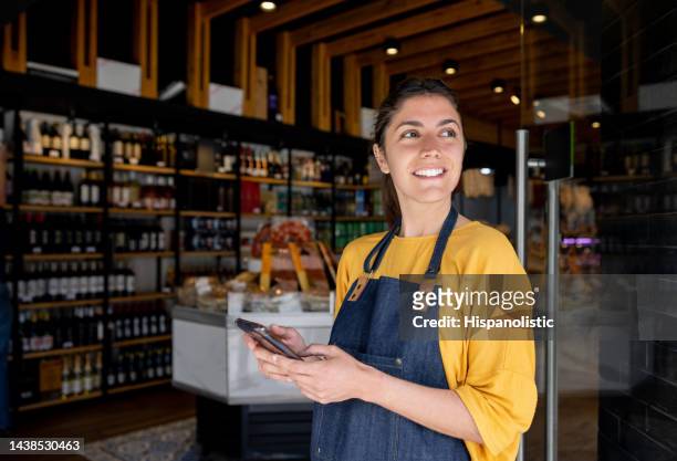 empleada minorista que trabaja en una tienda de alimentos y usa su teléfono celular mientras espera a los clientes - market vendor fotografías e imágenes de stock