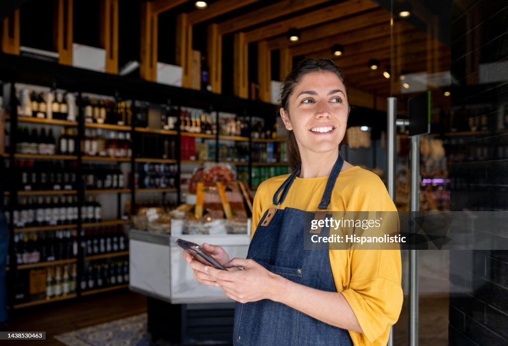 Retail clerk working at a food shop and using her cell phone while waiting for customers