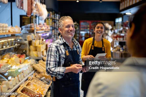 happy business owner talking to some employees at a supermarket - delicatessenzaak stockfoto's en -beelden