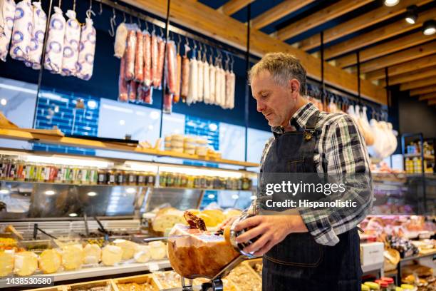 homme travaillant dans une charcuterie vendant des jambons et coupant une tranche de prosciutto - charcuteria photos et images de collection