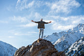 Hyped man standing on a rock surrounded by snowy mountains and sky