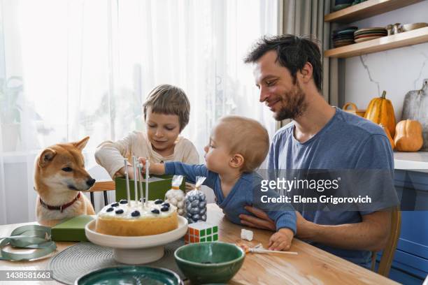 dad and his three sons and ginger dog celebrate birthday in a brightly lit kitchen with homemade cake - 40 birthday foto e immagini stock
