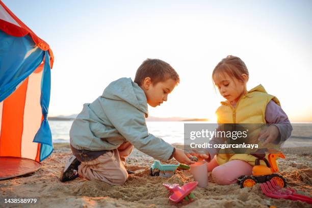 kleines mädchen und junge spielen mit plastikspielzeug am strand - kind sandburg stock-fotos und bilder