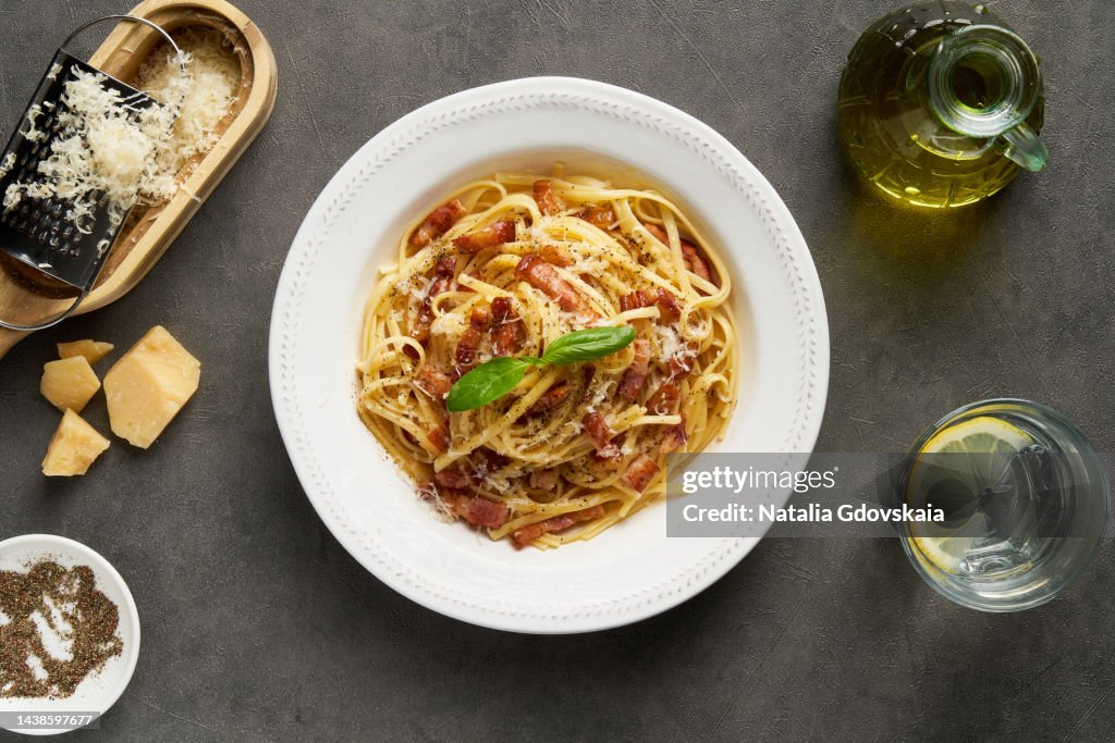 Carbonara pasta. Spaghetti with pancetta, egg, pepper,parmesan cheese and cream sauce. Cheese grater, olive oil, glass of water on table. Traditional Italian cuisine. Top view.