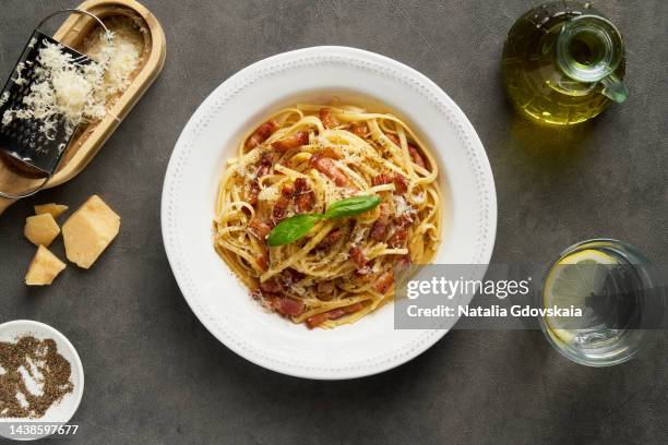 carbonara pasta. spaghetti with pancetta, egg, pepper,parmesan cheese and cream sauce. cheese grater, olive oil, glass of water on table. traditional italian cuisine. top view. - carbonara stock pictures, royalty-free photos & images