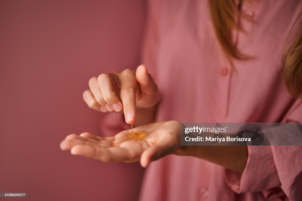 A girl in pink touches a gel cosmetic in her palm with her finger.