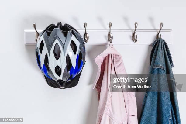 coat hooks on a white wall with denim jackets and cycling helmet on. - cycling helmet stock pictures, royalty-free photos & images