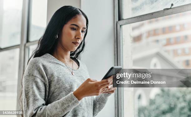 search, news and phone with woman by window for social media, internet and communication. contact, networking and app with girl and mobile at home thinking for digital, website and technology - using phone stock pictures, royalty-free photos & images