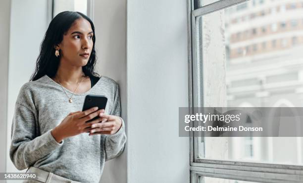 frau, telefon und denken durch fenster für kommunikation, 5g-netzwerk und angst vor social media fake news. ernsthafte frau in stadtwohnung mit smartphone, die unglücklich über online-mobbing-chat aussieht - fake news stock-fotos und bilder
