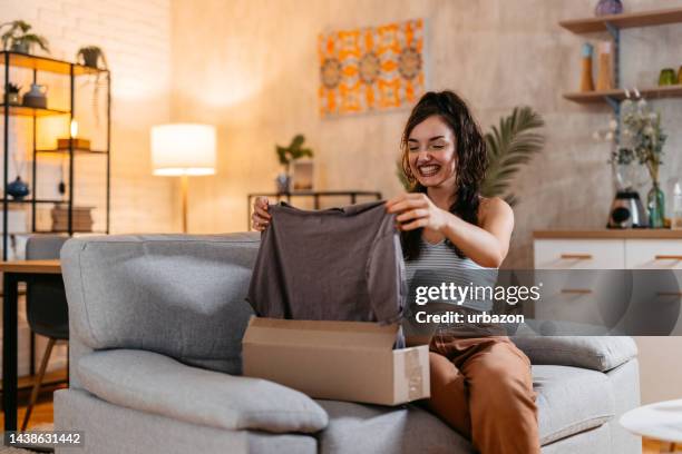 young woman unboxing a package with a new shirt - online shopping opening package stock pictures, royalty-free photos & images