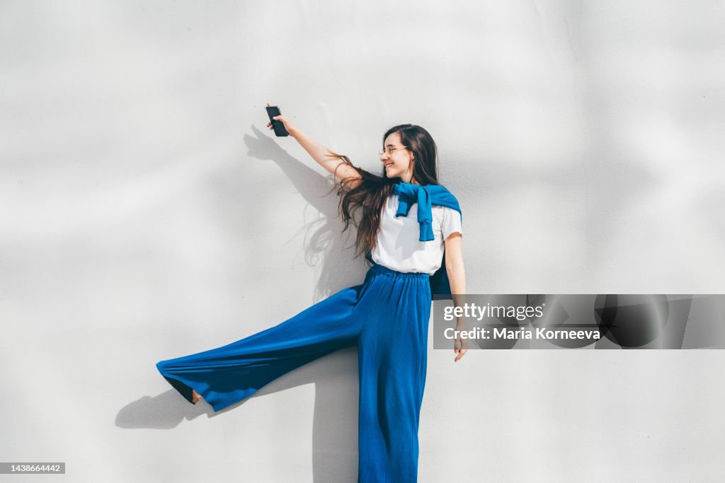 Woman using mobile phone in front of concrete wall. Happy woman with arms outstretched.