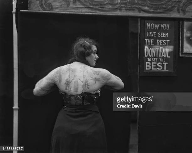 Rear view of a tattooed lady, beside a sign reading 'Now you've seen the rest don't fail to see the best' at the Royal Victory Circus & Allied Fair',...