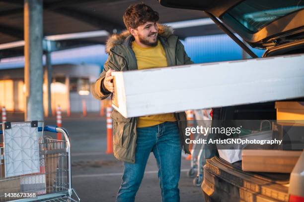 man loading tv set in car from a black fraday sale. - money to burn stock pictures, royalty-free photos & images