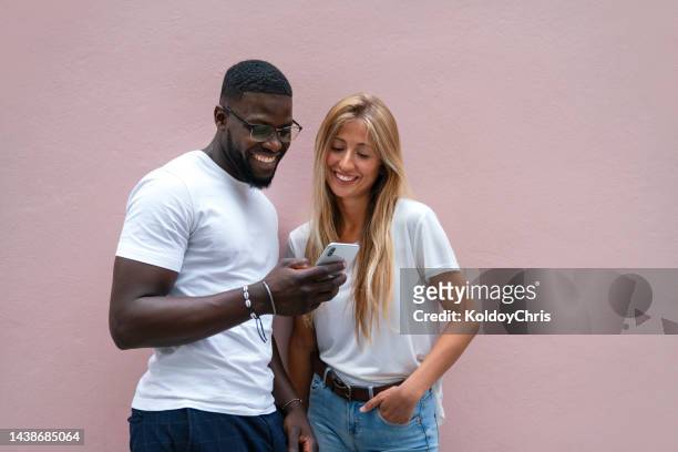 multiracial friends using phone against a pink wall outdoors - happy man pink background stock pictures, royalty-free photos & images