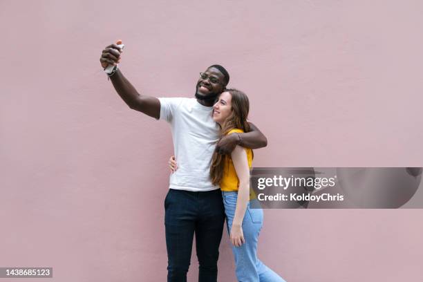 a young man taking a selfie with her girlfriend with a pink background - call to arms stock pictures, royalty-free photos & images