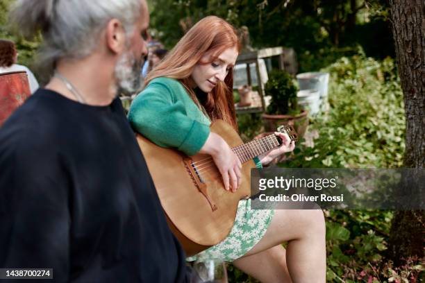 young woman with man in garden playing guitar - acoustic guitarist stock pictures, royalty-free photos & images