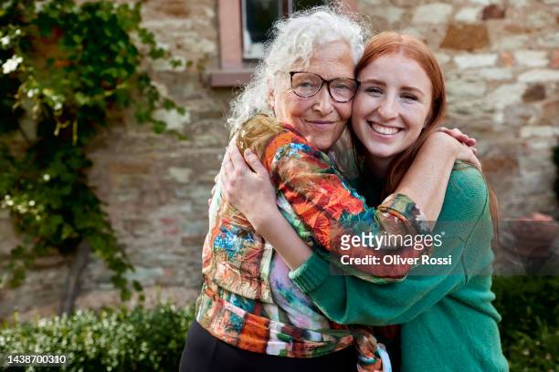 portrait of happy young woman and senior woman hugging in garden - young woman with grandmother stockfoto's en -beelden