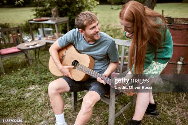 young man playing guitar for woman in garden - acoustic guitar stock-fotos und bilder
