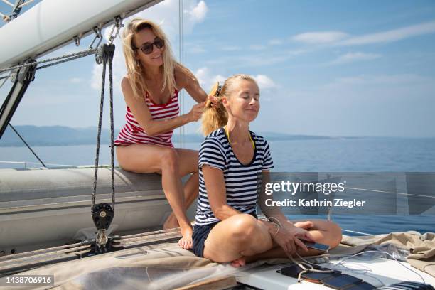 woman brushing her friend's hair on a sailboat - rayas marineras fotografías e imágenes de stock