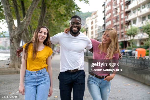 young friends walking together in the city - dreiviertel vorderansicht stock-fotos und bilder