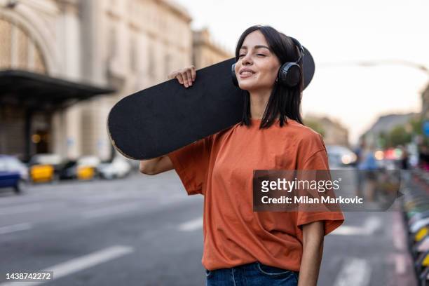 a young spanish woman with a skateboard walks down the street - model tshirt stockfoto's en -beelden