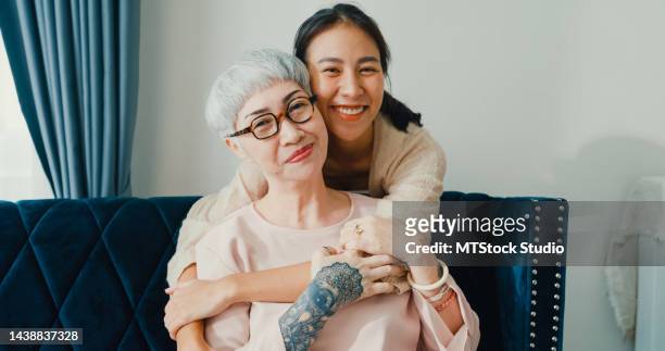 happy young asian daughter and retirement senior mother sit at cozy sofa couch hug fun enjoy family moment at home. - respect trust stock pictures, royalty-free photos & images