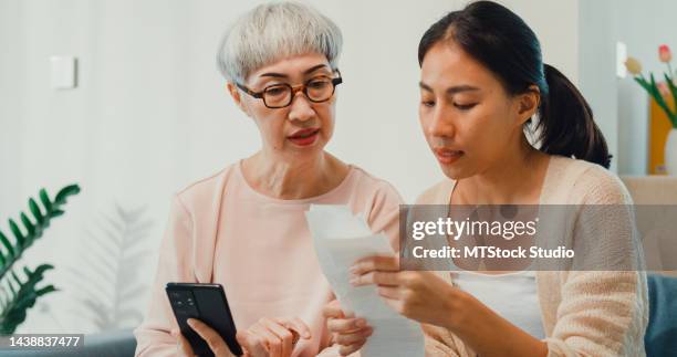 happy asian family, young daughter and senior elderly mom sit on couch teach older mother to use smartphone how to pay online payment facility bill at home on weekend. - grandma invoice bildbanksfoton och bilder