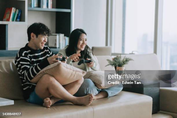 asiatische chinesische lgbtqia schwuler mann genießt videospiel mit freundin im wohnzimmer - jugendkultur sitzen konsole stock-fotos und bilder