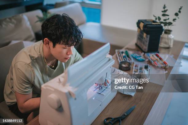 asian chinese gay man sewing with sewing machine at home in living room - side hustle stock pictures, royalty-free photos & images