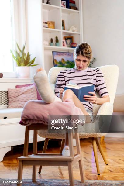 young woman with leg in plaster reading book - broken leg stock pictures, royalty-free photos & images