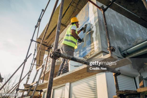 un ouvrier de la construction construit la façade d’un bâtiment - façade photos et images de collection